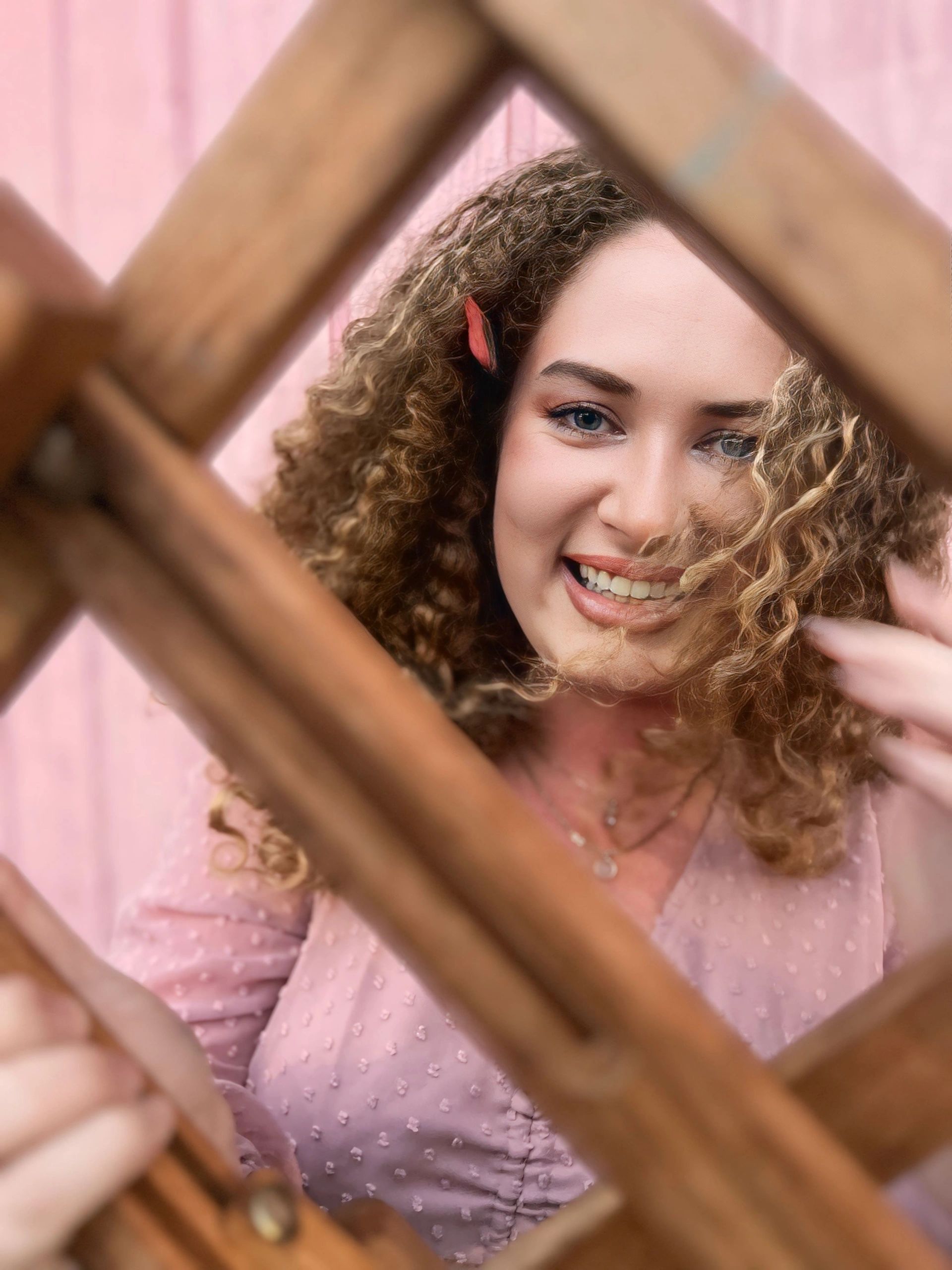 Katie smiling, framed by a wooden lattice against a soft pink wall