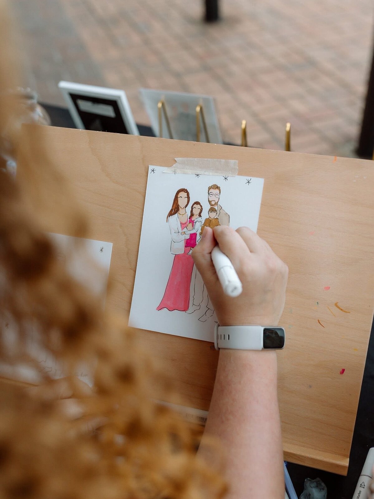 Katie sketching a family in marker at an event, the illustration taped to her drawing board