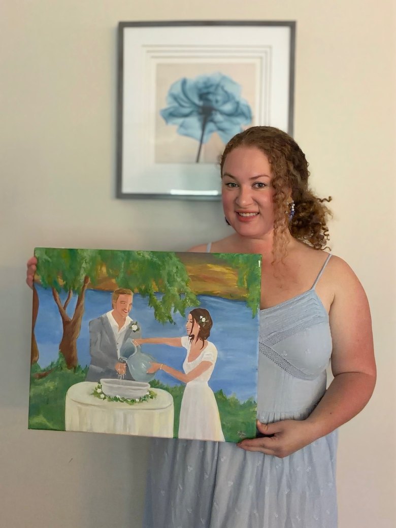 Katie holding a live wedding painting of a couple's water ceremony beneath a willow by the lake