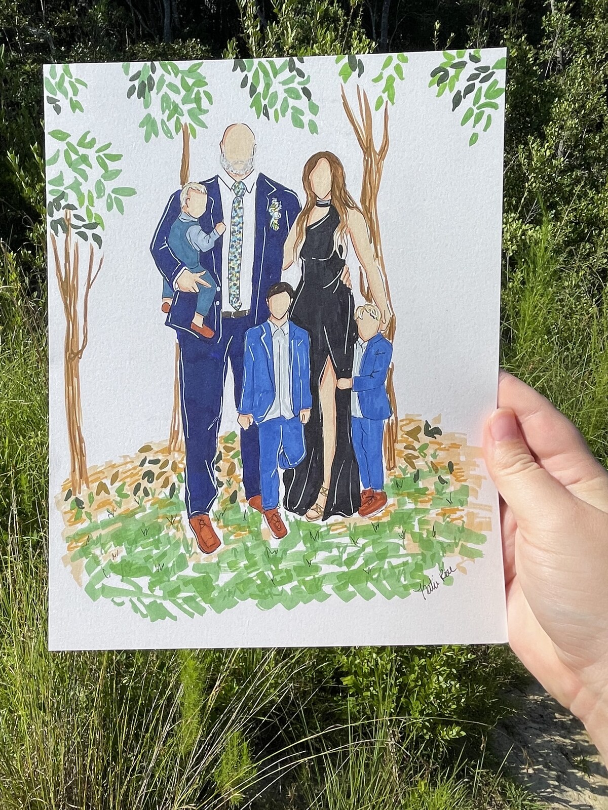 A hand-drawn family portrait held up among the trees where it was painted